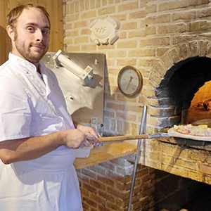 Le cuisinier de l'auberge devant son four à pizza et une pizza